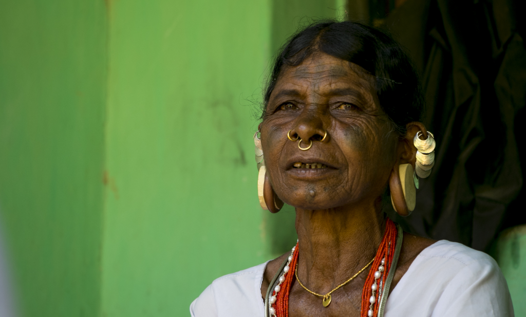 Authentic portrait of a Sora elder woman with traditional nose rings, wooden ear plugs, facial tattoos, and beaded necklaces in Odisha